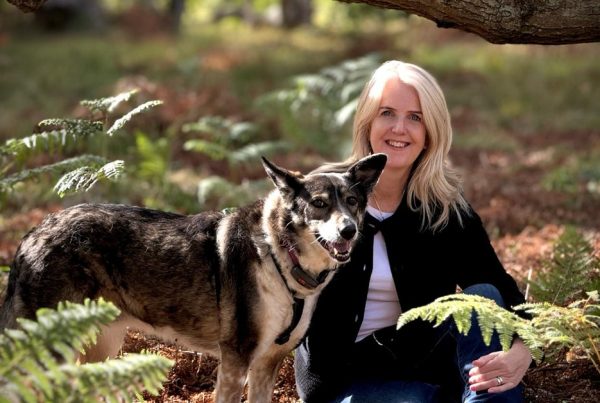 Animal communicator Pea Horsley sitting with her dog among the ferns in a woodland