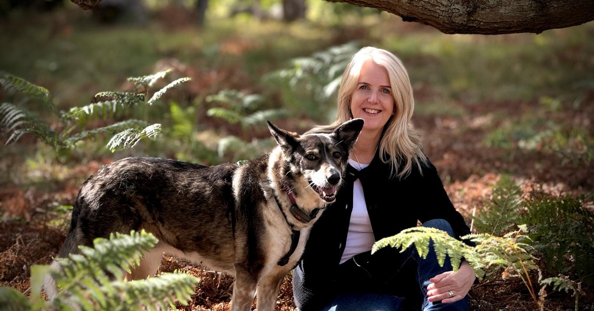 Animal communicator Pea Horsley sitting with her dog among the ferns in a woodland